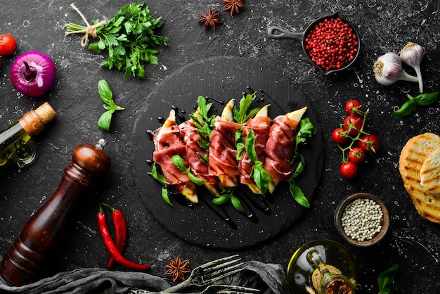 Prosciutto con pere e basilico su una lastra di pietra nera jamon antipasto italiano vista dall'alto