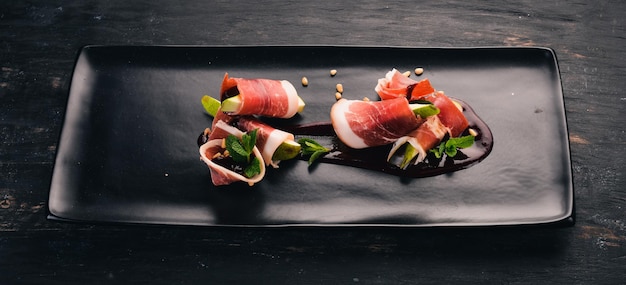 Prosciutto with pear and berry sauce cold snacks top view on a\
black wooden background copy space