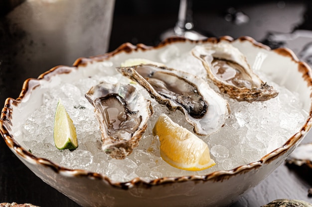 Prosecco bar concept. Open oysters lie on crushed ice with lemon and lime, next to a glass of champagne. Background image. Copy space.