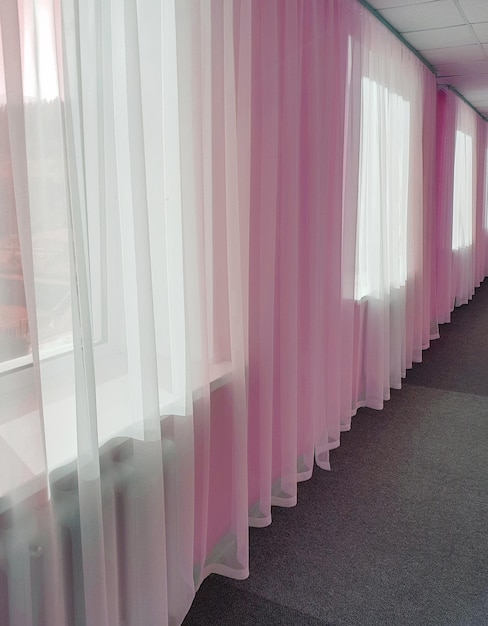 The prospect of a long hotel corridor with transparent curtains on large windows and pink tinting