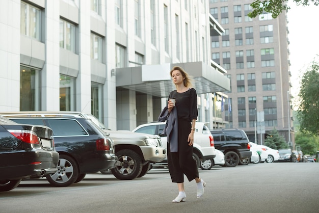 Prosperous female manager holding coffee to go cup strolling on the city street