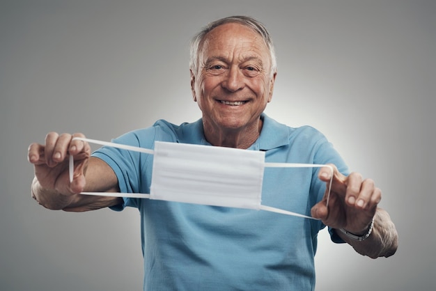 Protect yourself this season Shot of an elderly man holding a protective face mask in a studio agains a grey background