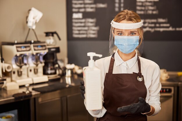 Protected coffee house worker showing sanitizing substance