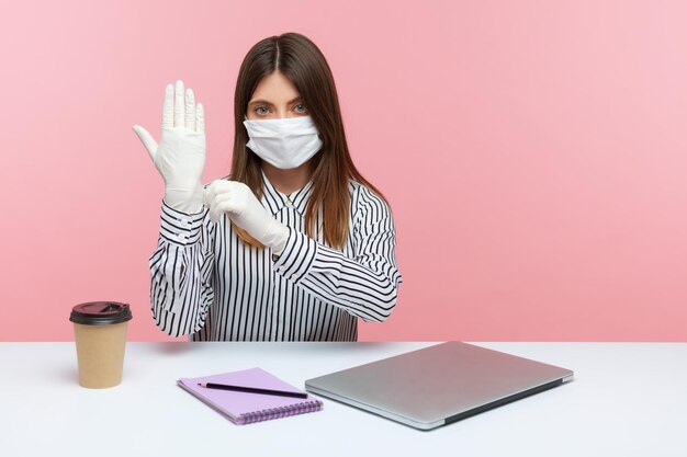 Protection against coronavirus infection Woman office employee sitting at workplace feeling safe healthy with hygienic face mask and protective gloves during covid19 quarantine indoor studio shot