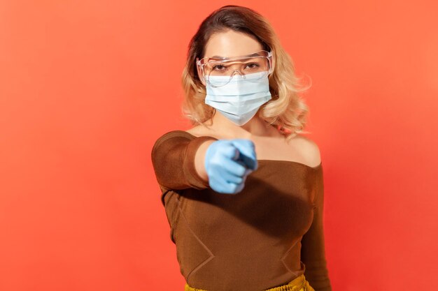 Protection against coronavirus. Woman wearing hygienic face mask, gloves and protective glasses, pointing finger to camera, giving recommendations to prevent viral disease, 2019-ncov pandemic threat