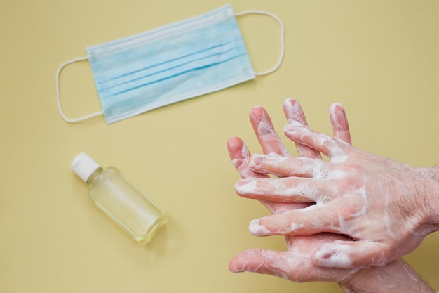 黄色の背景に石鹸と手指消毒剤で手を掃除するウイルス発生の概念の人の間の保護