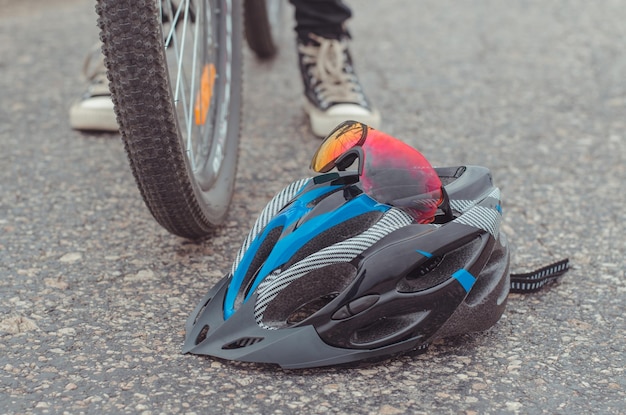 保護用の自転車用ヘルメットとゴーグルは、自転車の近くのアスファルトに横たわっています