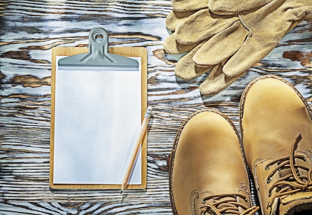 Protective boots leather gloves pencil clipboard on wooden board.