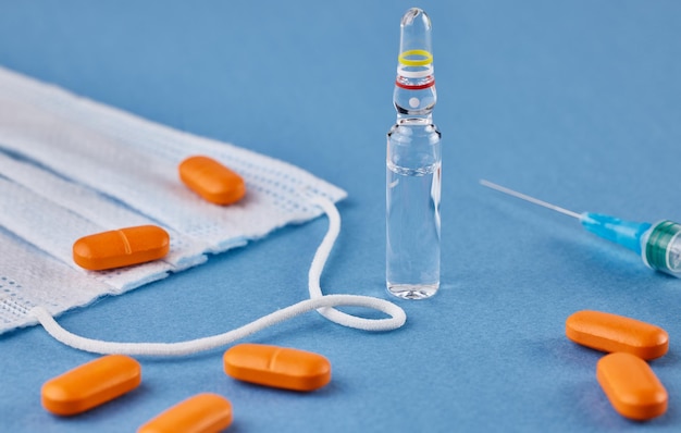 Protective face mask orange pills ampoule and syringe on a blue background The concept of illness