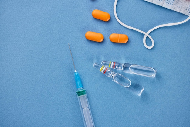 A protective face mask orange pills two ampoules of medicine and a syringe on a blue background