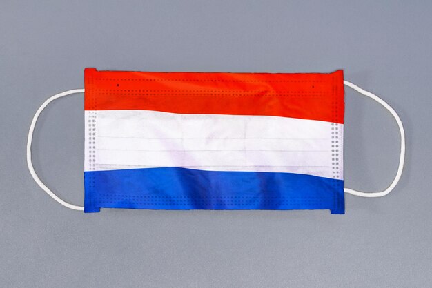 회색 배경에 네덜란드의 국기가 있는 보호 거즈 마스크 회색 배경에 의료 보호 마스크
