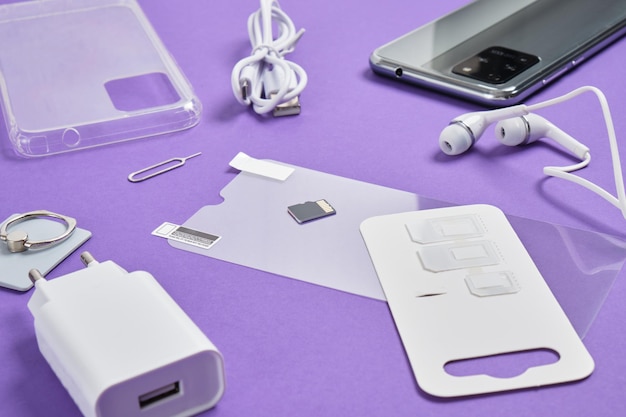 Protective glass, case, charger, headphones for a smartphone, slots for sim cards on a purple background smartphone accessory