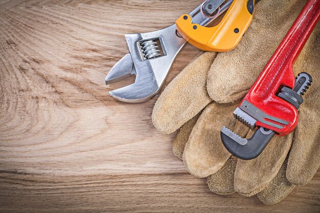 Protective gloves adjustable key monkey wrench pipe cutter on wooden board plumbing concept.