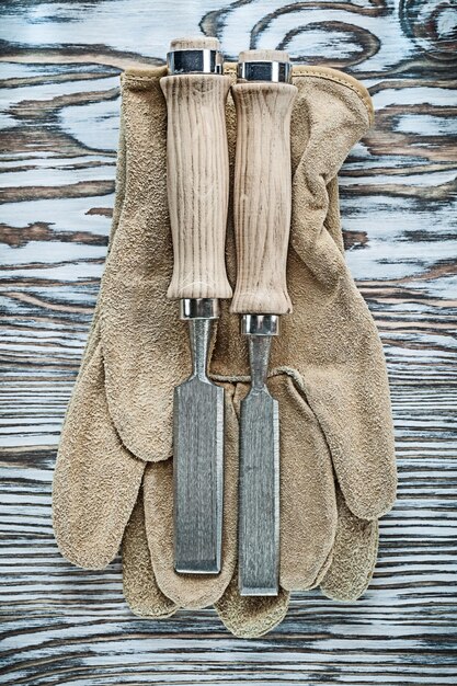 Protective gloves flat chisels on wooden board.