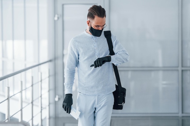 In protective mask and gloves Young handsome man in formal clothes indoors in the office at daytime