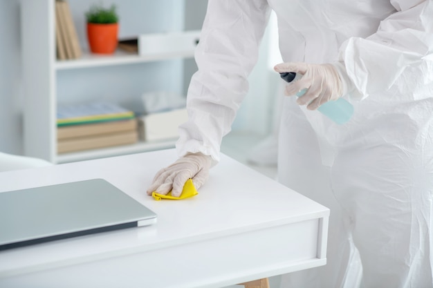 Protective measures. Close-up of medical worker hands in gloves spraying disinfectant on table