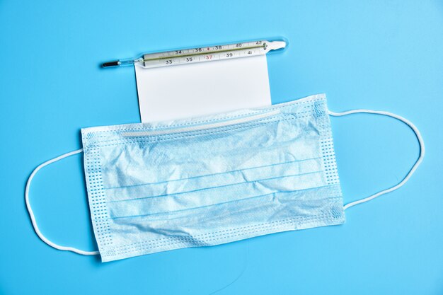 Protective medical face mask. Thermometer and white card on a blue background.