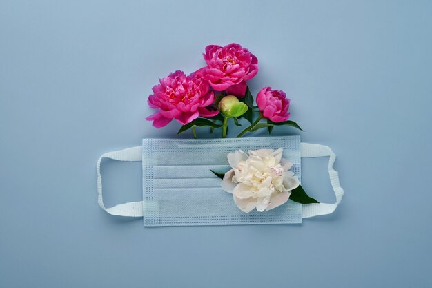 Protective medical face mask with peonies flowers on blue\
background. disposable surgical mask as symbol of coronavirus or\
covid-19 pandemic protection. valentine, women or mother day\
concept.