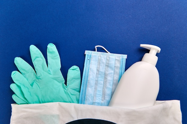 Protective medical mask, sanitizer gel and gloves in white bag. Protective measures against virus, coronavirus, bacteria, Flat lay. Copy space.
