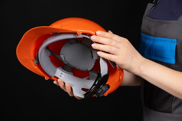 Photo protective orange helmet in the hands of a female builder on a black background