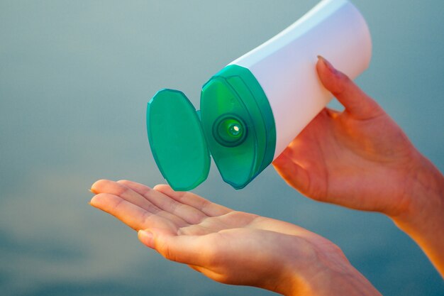 Crema solare protettiva sull'oceano nelle mani di una ragazza.