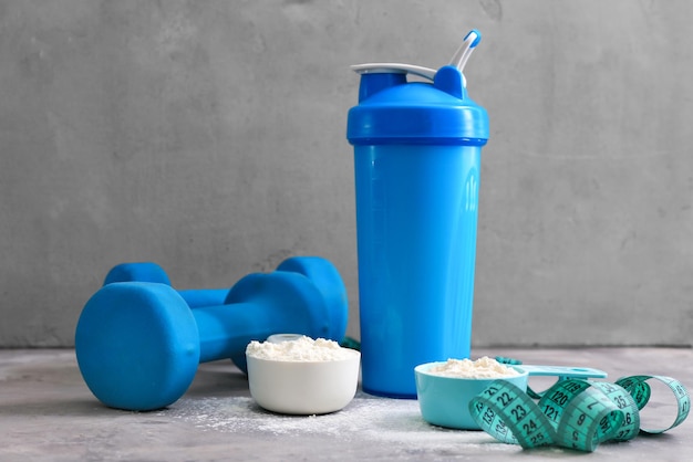 Protein shake in bottle powder measuring tape and dumbbells on table