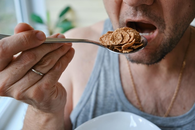 Photo protein and vitamins man at home room eating natural vegetarian granola buckwheat flakes closeup of an unrecognizable man