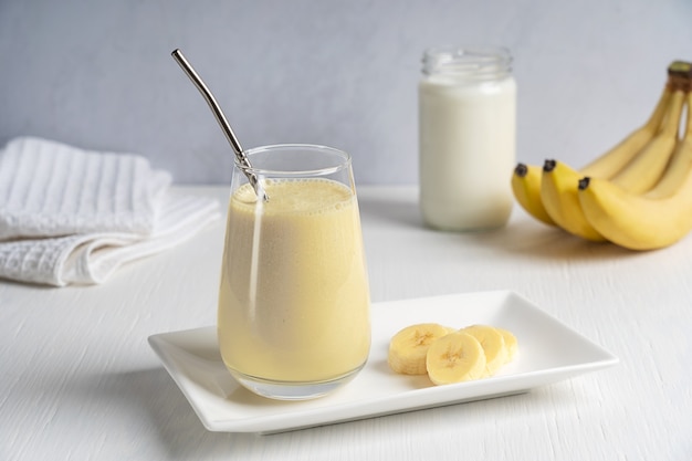 Proteïne-energie bananenmilkshake geserveerd in drinkglas met metalen rietje op witte houten tafel