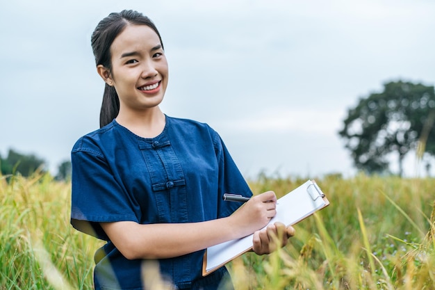 田んぼでの作業中にクリップボードに書いているProtraitアジアの若い農夫の女性