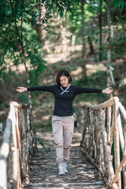 Protrait young woman standing on bamboo bridge smile and looking beautiful nature while camping in forest with happy copy space