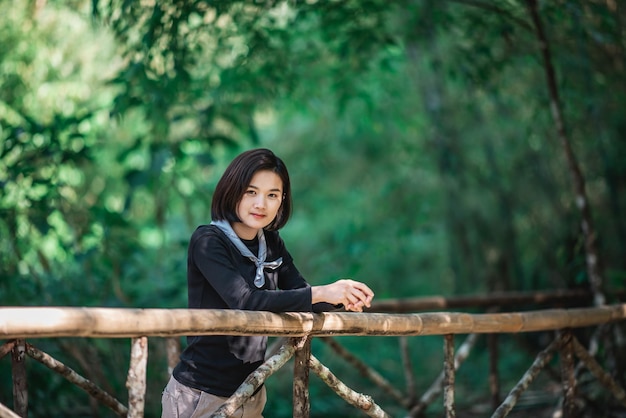 Protrait young woman standing on bamboo bridge smile and looking beautiful nature while camping in forest with happy copy space