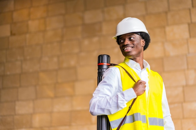 Proud african architect wearing helmet and waistcoat holding a drawing tube