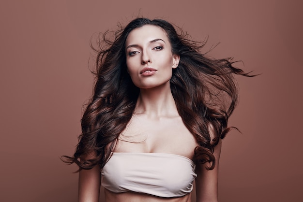 Proud to be beautiful. Attractive young woman looking at camera while standing against grey background