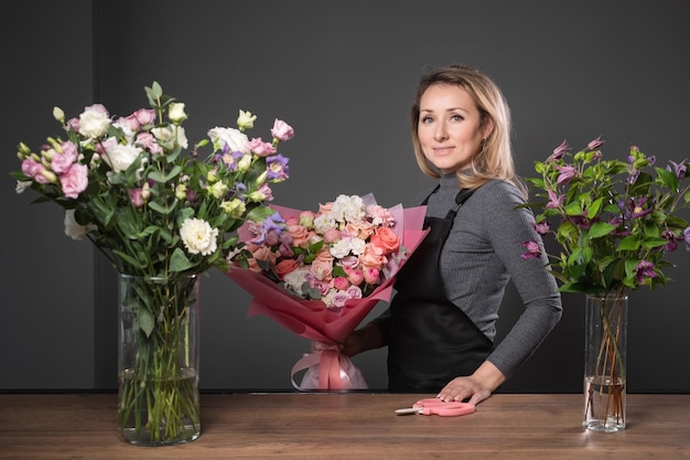 誇り高き花屋のブロンドの女性は、構成された花の花束を保持します