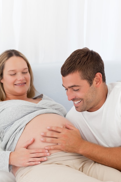 Proud future dad touching the belly of his wife lying on the bed