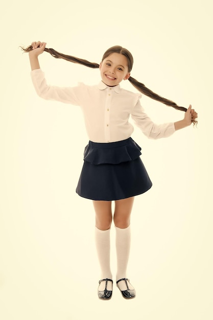 Proud of her long hair Kid girl charming ponytail hairstyle cute happy white background Child formal outfit school uniform Kid stylish fashionable posing holds her long curly hair ponytails