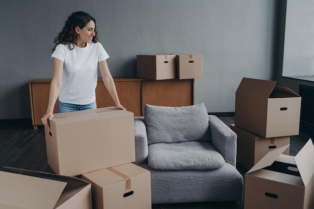 Proud single european lady in casual outfit moves cardboard\
boxes on floor real estate purchase