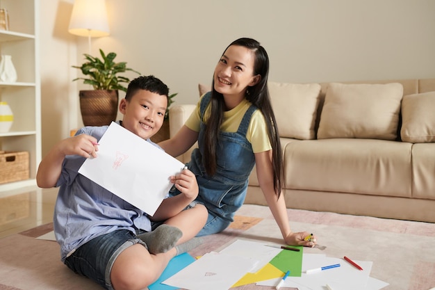 Proud smiling preteen boy showing picture he drawn with his mother