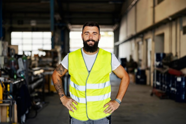 A proud worker in vest standing with hands on hips at workshop