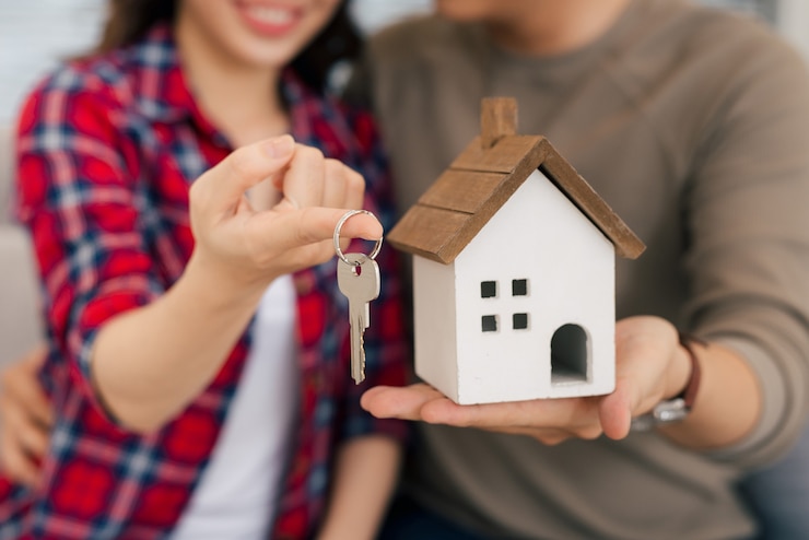 Photo proud young asian couple with keys and wooden house modelling