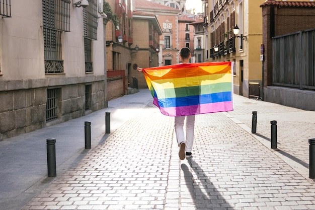 Proudly Embracing the LGBT Flag a Backlit Man Stands with Open Arms on a Sunny City Street at Sunset
