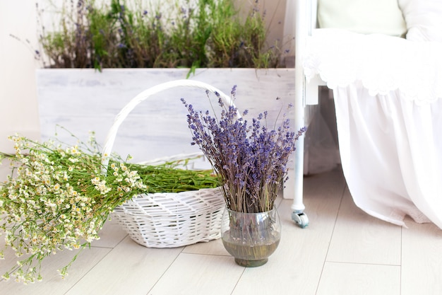 Provence, rustieke stijl, lavendel! Een grote mand met veldmadeliefjes en een vaas met lavendel staan op de vloer in de slaapkamer. Aromatherapie. Het concept van zomervakantie in platteland.