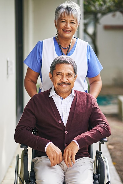Photo providing assistance with a smile portrait of a senior man in a wheelchair being cared for by a nurse at a retirement home