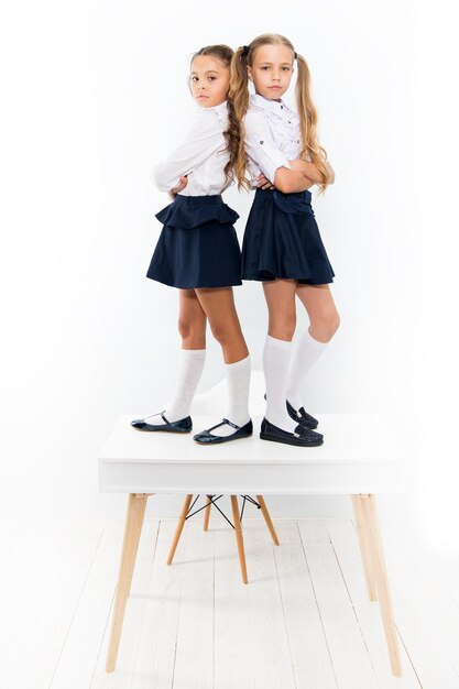 Providing children with education Small children standing on table in classroom Little children enjoying school break Cute children with long hair wearing school uniform with fashion look