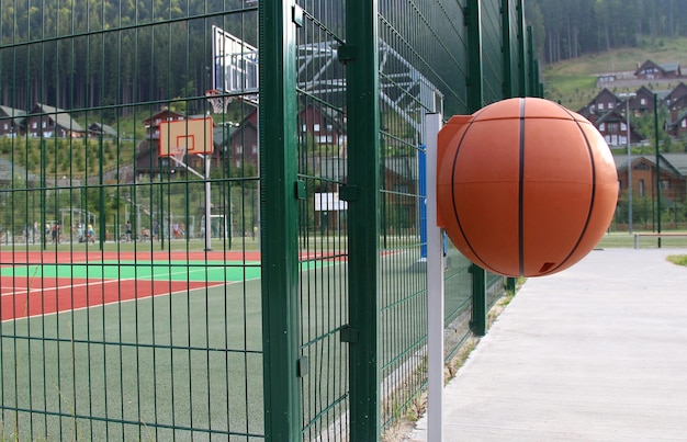 Prullenbak in de vorm van een basketbalbal op een voetpad bij buitensportclub