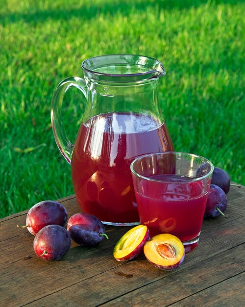 Prune juice in the carafe and glass with plums natural background in sunny day