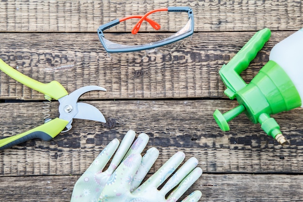 Pruner, pressure sprayer, garden gloves and protective glasses on wooden board. Garden tools and equipment