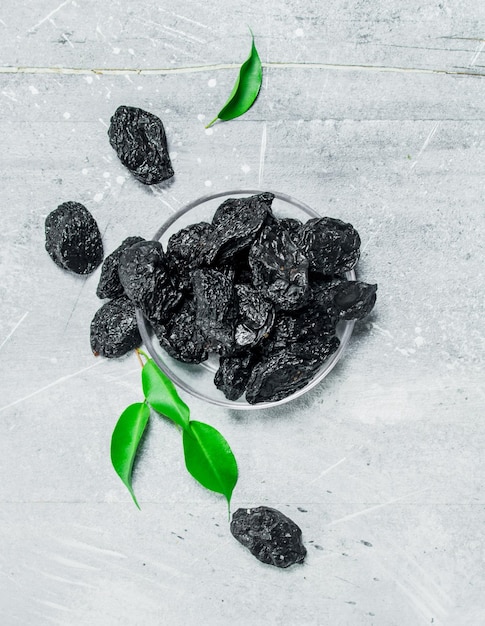 Prunes in a bowl with green leaves