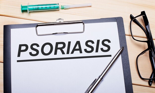 PSORIASIS is written on a white piece of paper next to black-rimmed glasses, a pen and a syringe. Medical concept