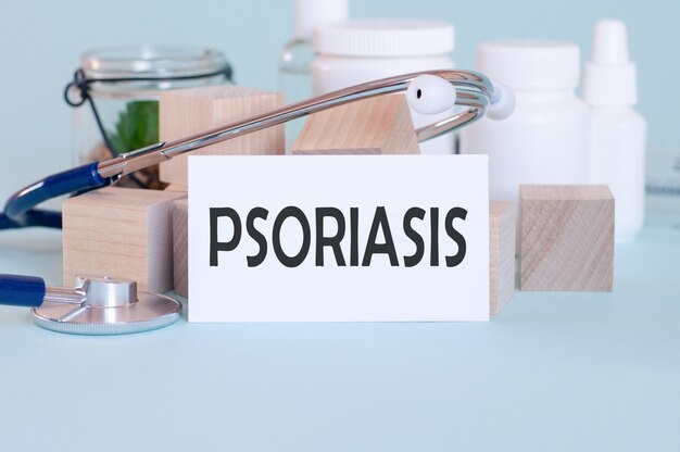 흰색 의료 카드에 쓰여진 PSORIASIS 단어, 의학 마스크, 청진기 및 벽에 녹색 꽃